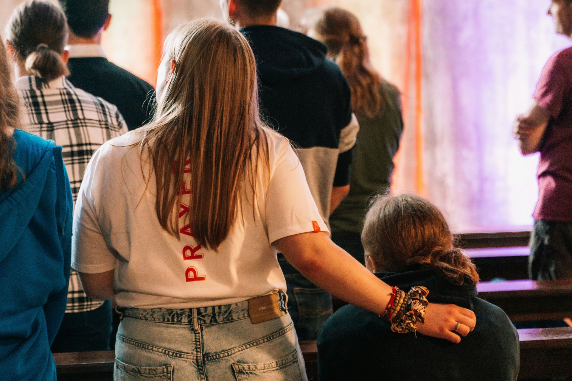 Ein Mädchen legt in einer Kirche den Arm auf die Schulter eines Freundes.